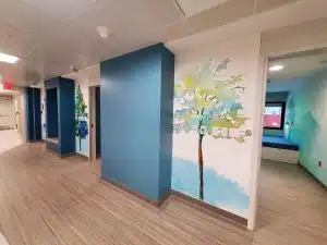 A hallway at the new mental health unit at Children's Minnesota which shows tree murals and entrances into rooms with beds for patients and their parent/caregiver.